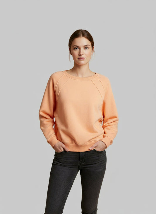 Woman wearing tangerine pullover with  black jeans on a neutral background