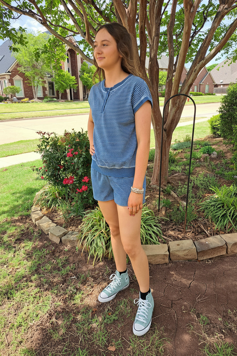 Person wearing a blue striped shirt and shorts standing outdoors near a tree