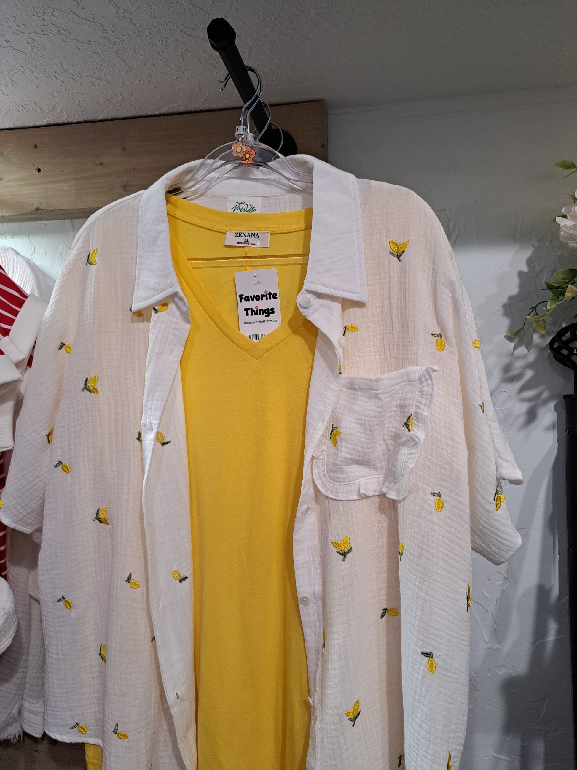 Yellow dress with white cover-up and lemon pattern on hanger against a neutral wall.
