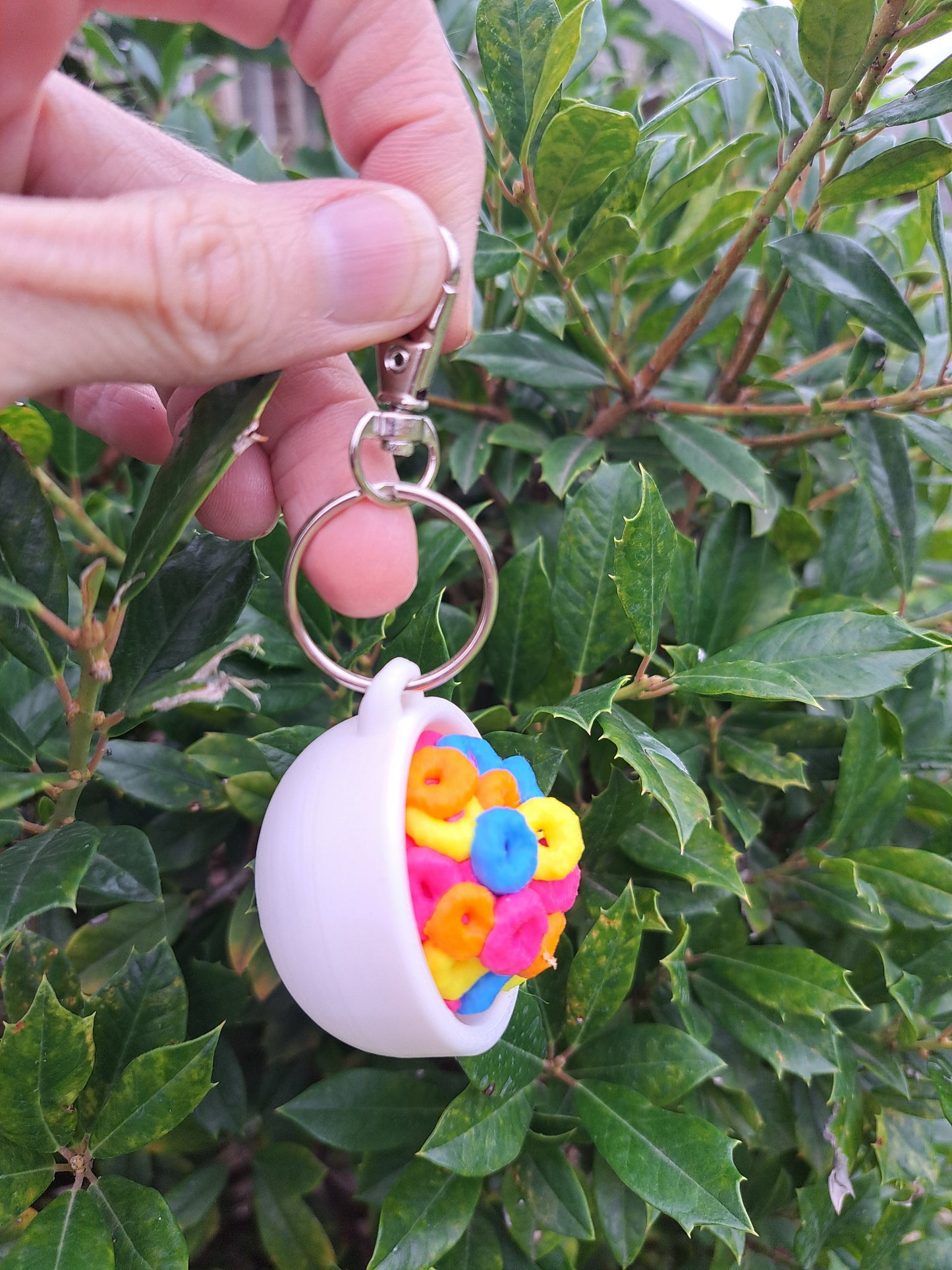 Keychain with colorful flower design held in front of green foliage