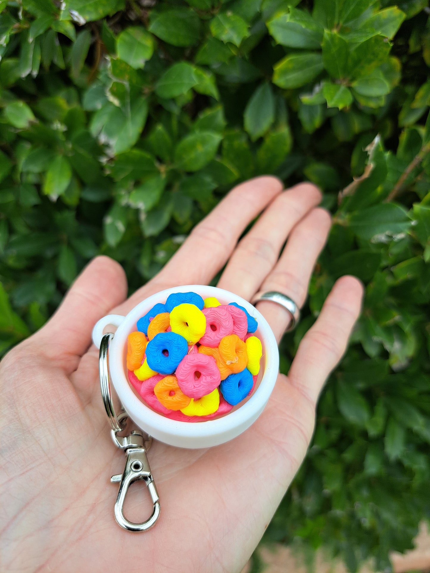 Hand holding a colorful keychain with a white base against a green leafy background