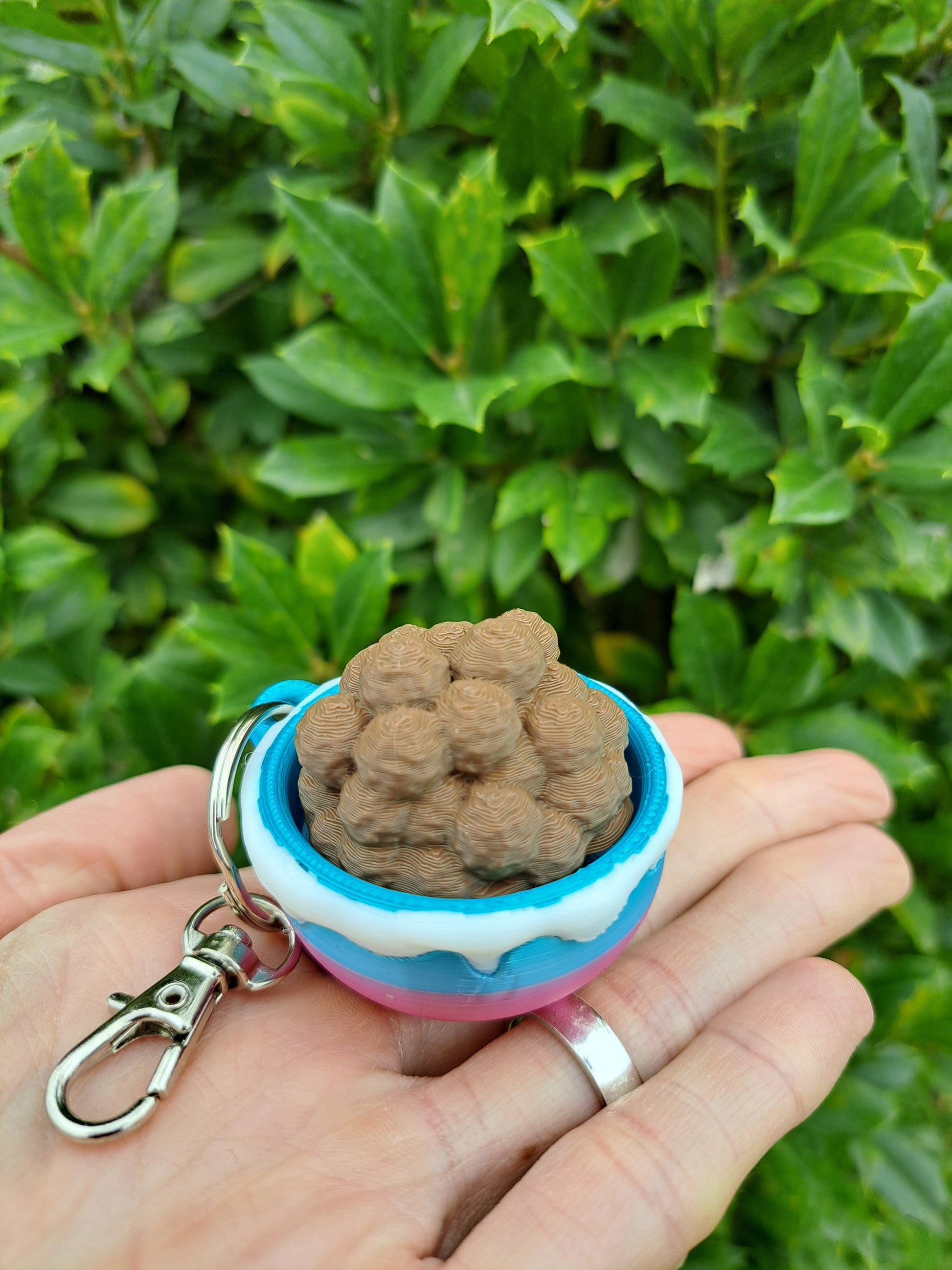 Keychain with a small object held by a hand against a green leafy background