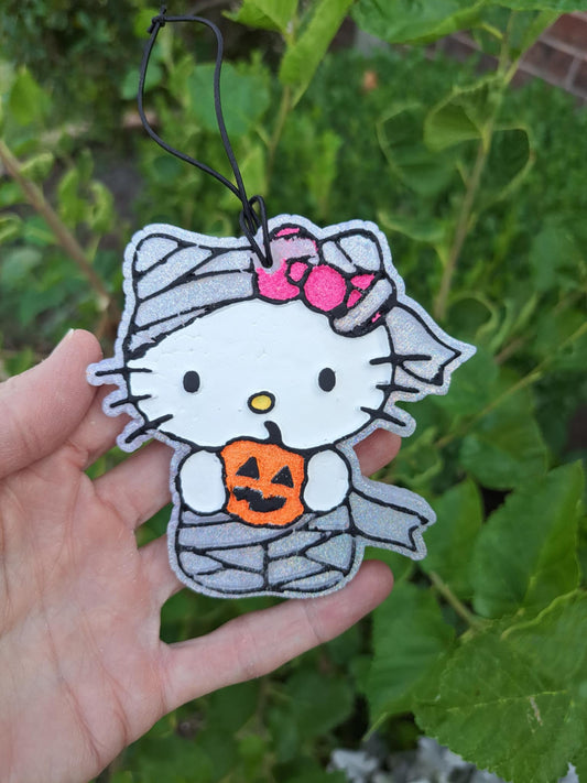 silver mummy kitty air freshener held by hand in front of greenery