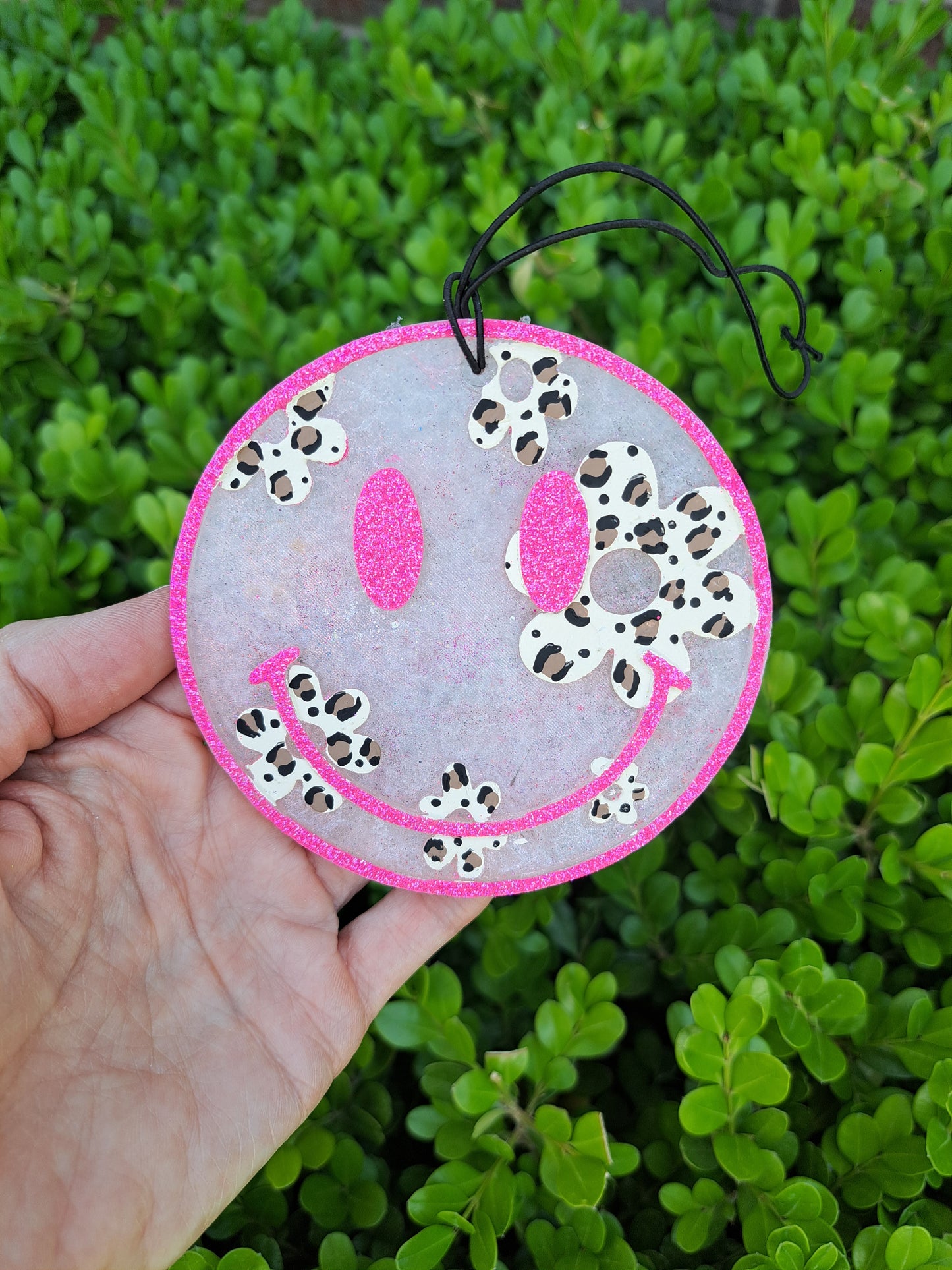 Smiley face ornament with leopard daisies held in front of green foliage