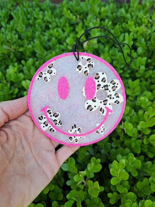 Smiley face ornament with leopard daisies held in front of green foliage