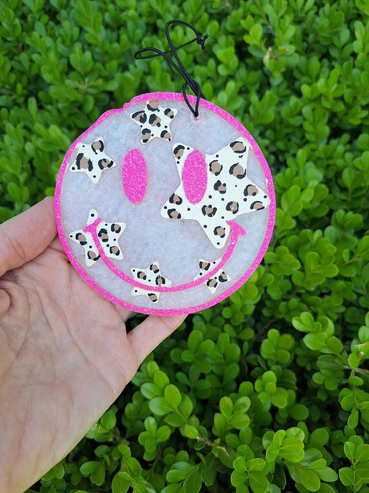 Smiley face freshie with leopard stars held in front of green foliage