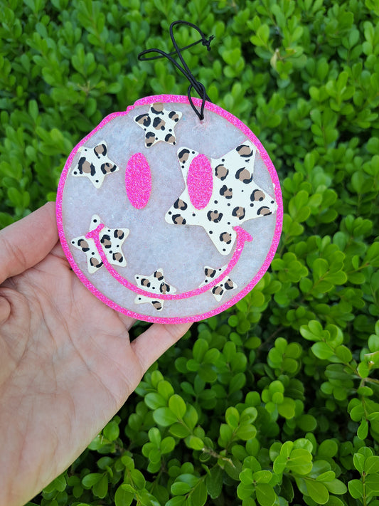 Smiley face freshie with leopard stars held in front of green foliage