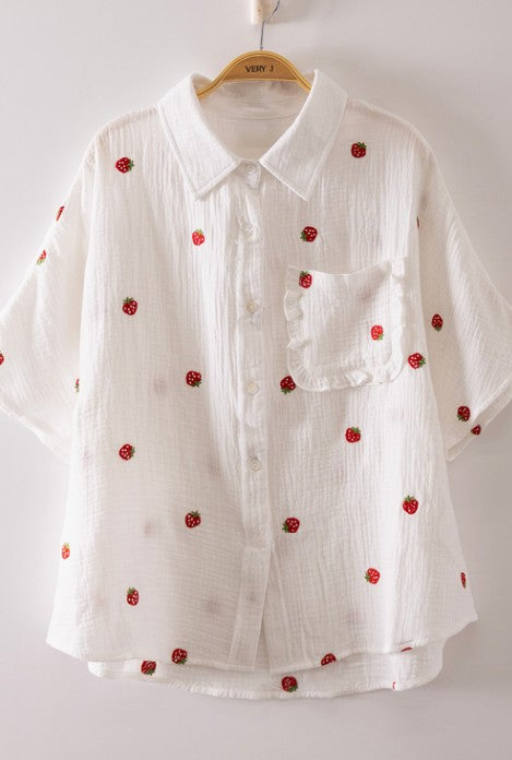 White shirt with red floral embellishments on a hanger against a white background