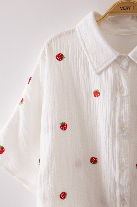 White shirt with red strawberry embroidery on a hanger against a white background