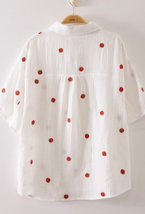 White blouse with red floral embroidery on a hanger against a white background