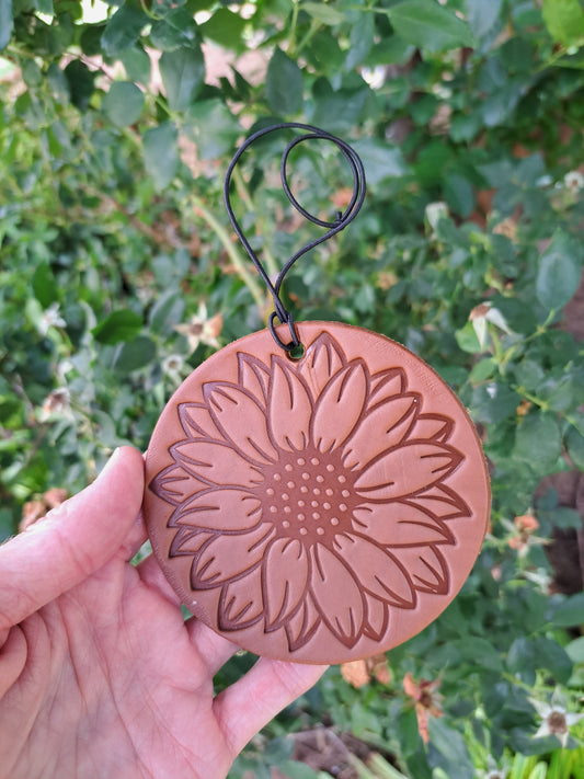 Hand holding a sunflower tooled round leather freshie against a green leafy background