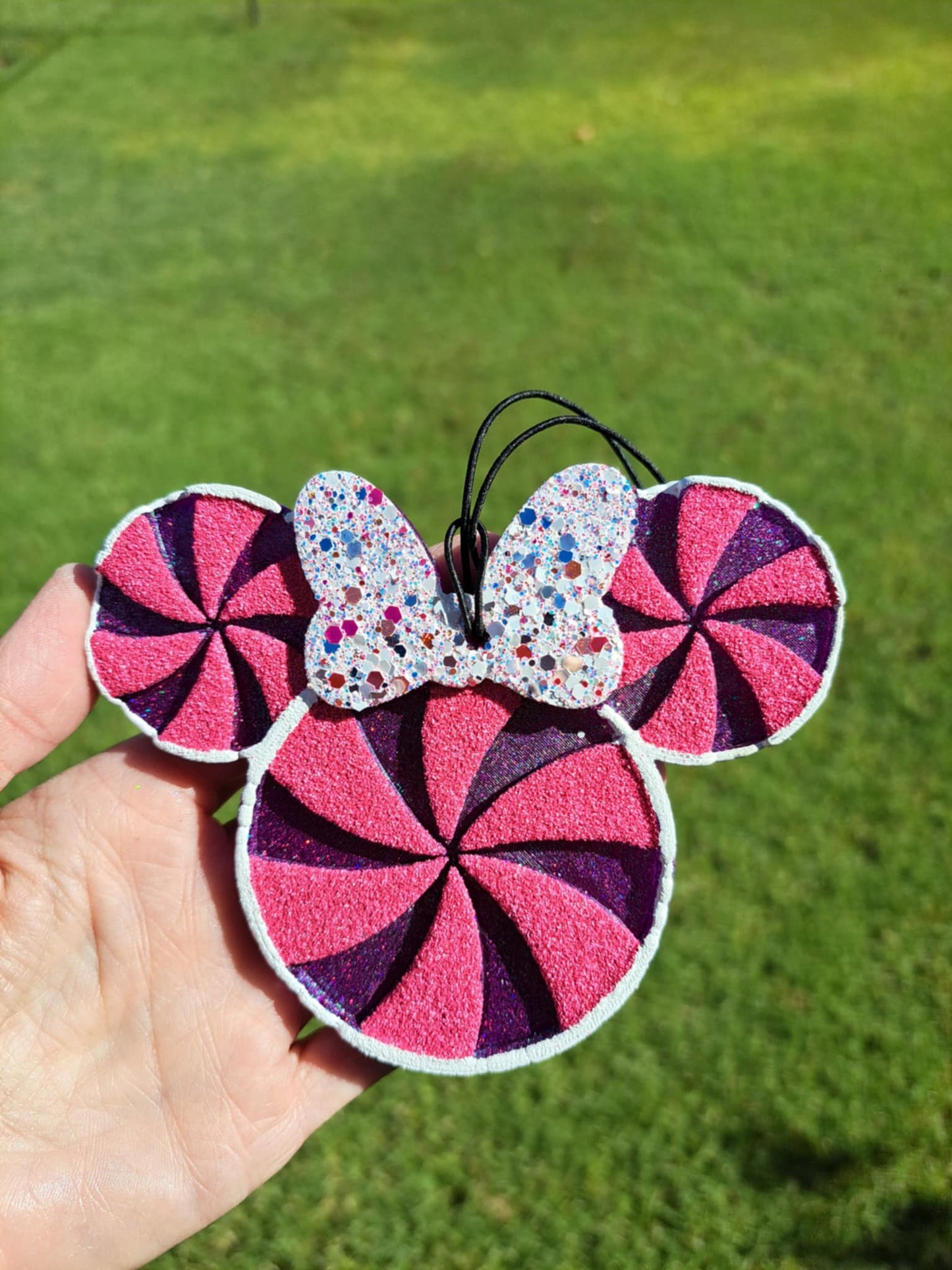 Pink and purple decorative freshie held in a hand against a green grass background