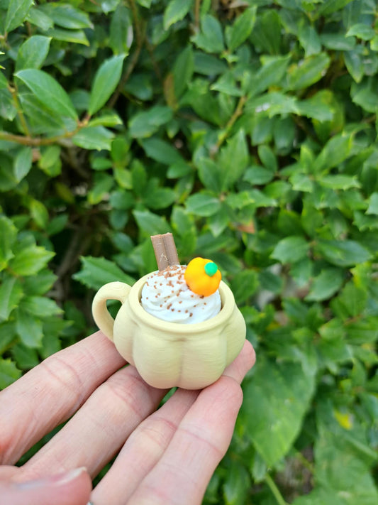 hand holding a small tan pumkin shaped mug 3D clicker fidget toy against a green background