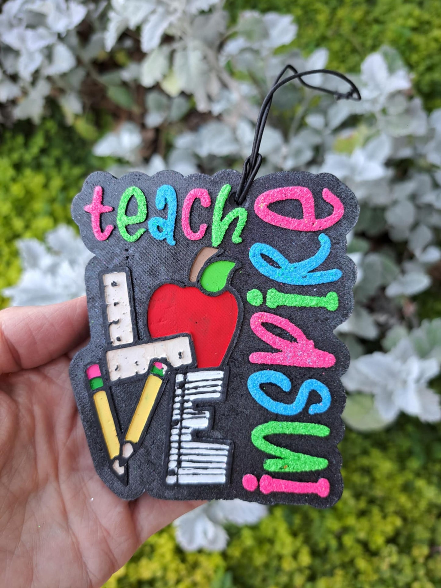 Colorful 'inspired teacher' freshie held by a hand in front of greenry background