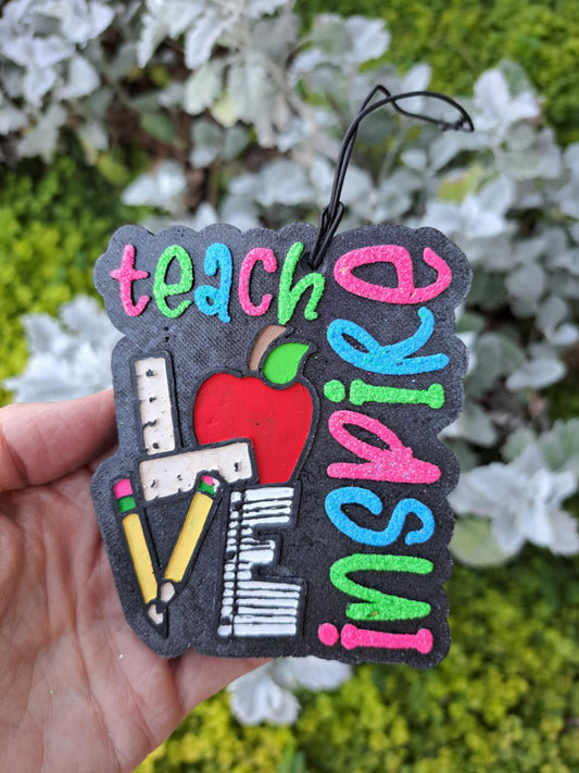 Colorful 'inspired teacher' freshie held by a hand in front of greenry background
