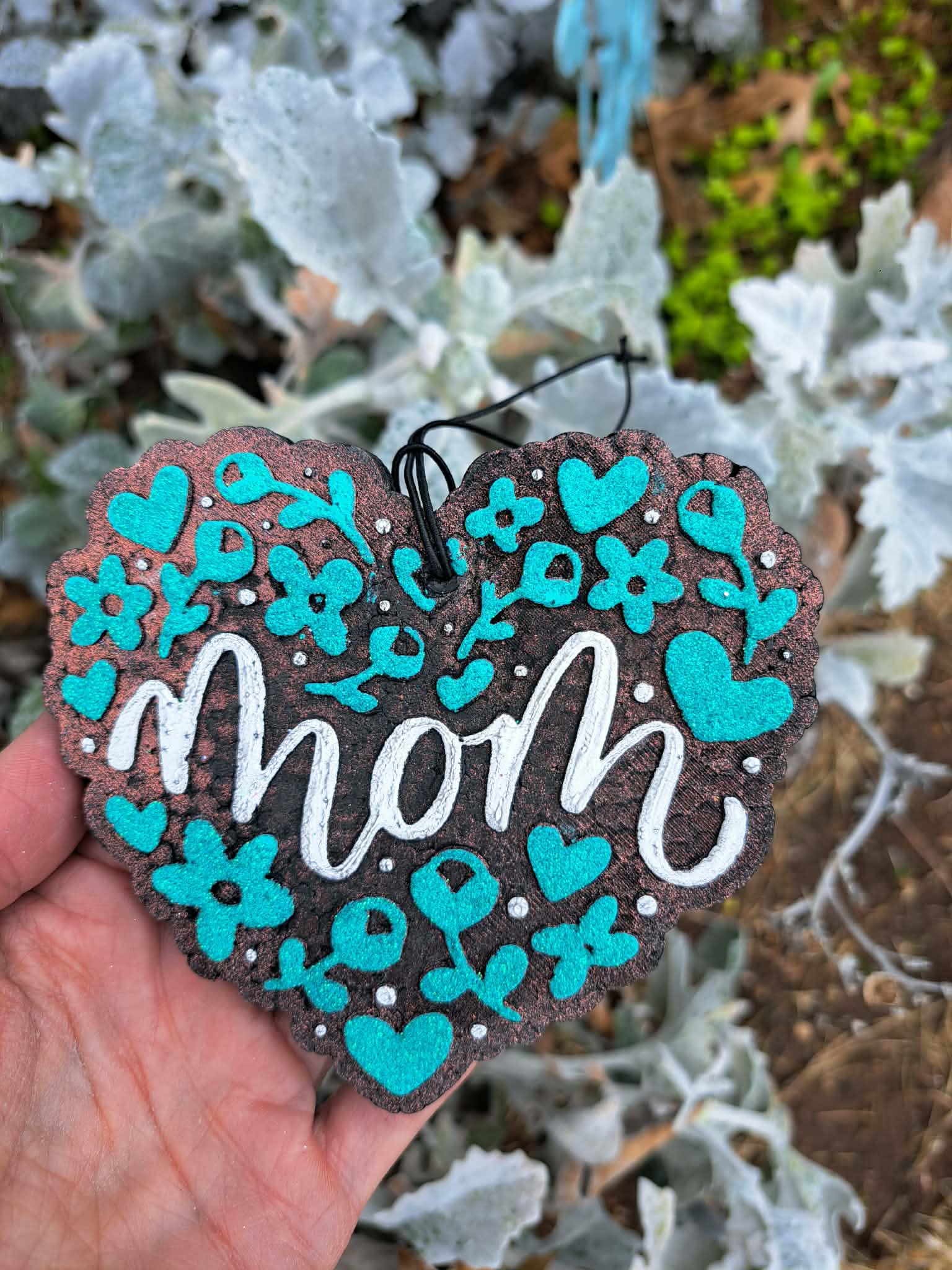 Heart-shaped freshie with 'mom' in white text surrounded by blue hearts against a natural background