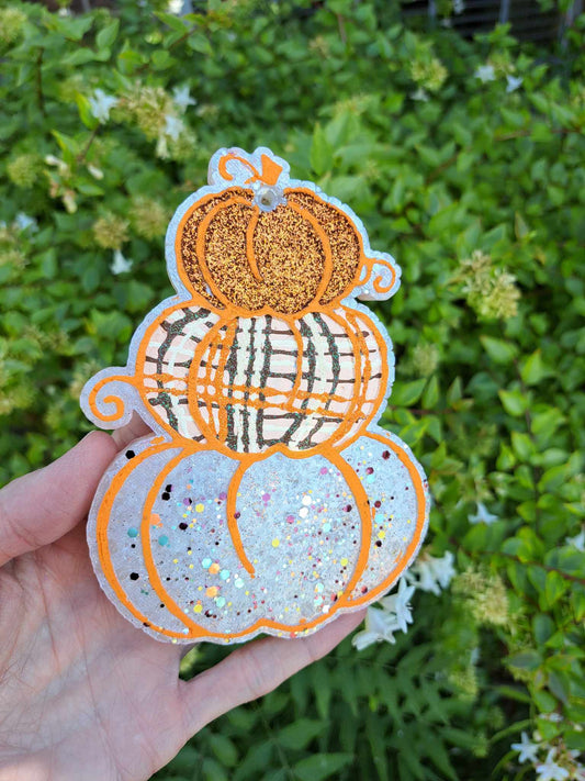 hand holding a freshie that looks like a stack of three pumpkins with the bottom one white, the center one painted plaid and the top one orange glitter