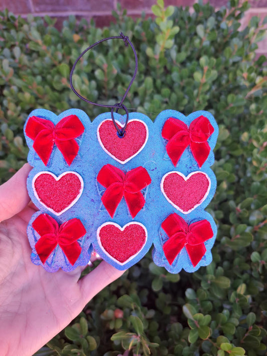hand holding a freshie with red bows and hearts on it against a green background