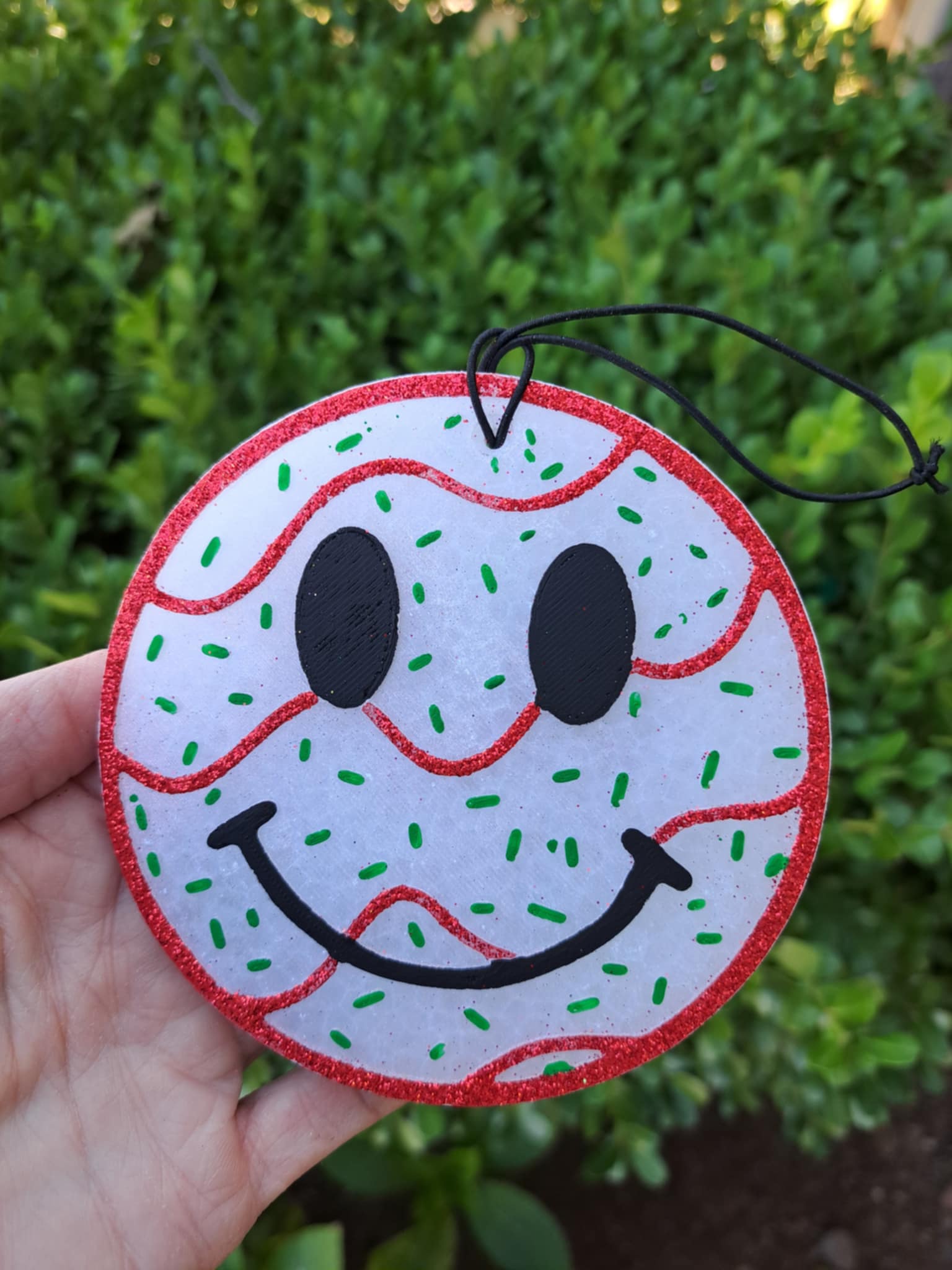 Circular smiley face tree cake freshie held in front of green foliage