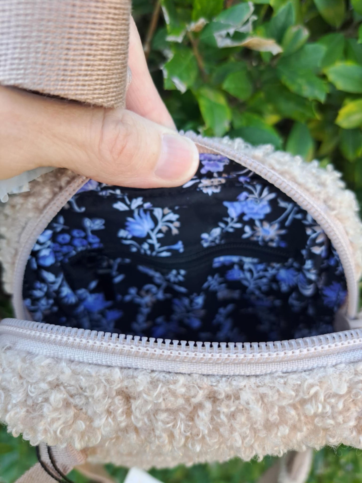inside of a crossbody bag with zipper across the back. leafy background