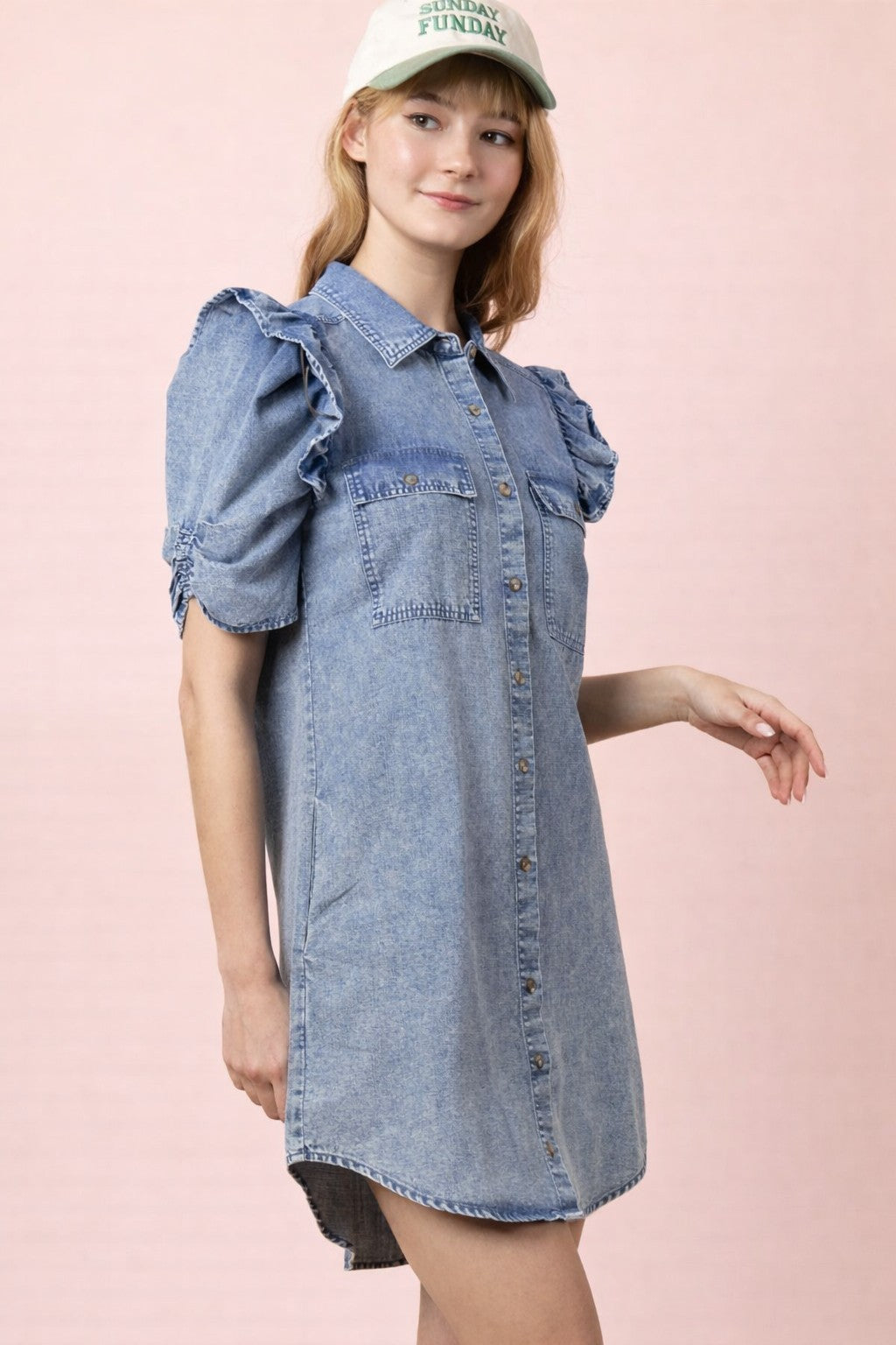 Woman wearing a denim dress with ruffled sleeves against a pink background