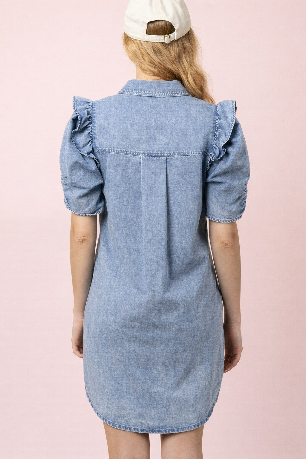 Person wearing a denim dress with ruffled sleeves on a pink background