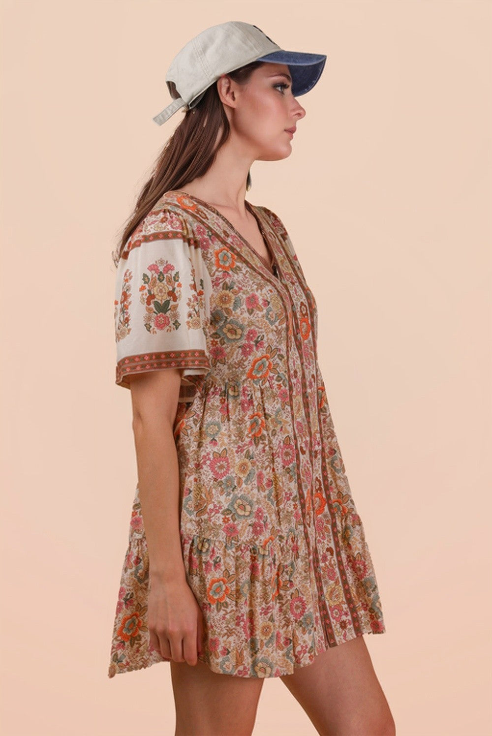 Woman wearing a floral dress and cap against a beige background