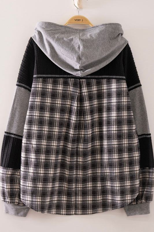 A hooded colorblock sweatshirt hanging on a wooden hanger against a plain white wall. The hoodie features a gray hood, black ribbed shoulder and sleeve sections, and a black, gray, and white plaid patterned body.