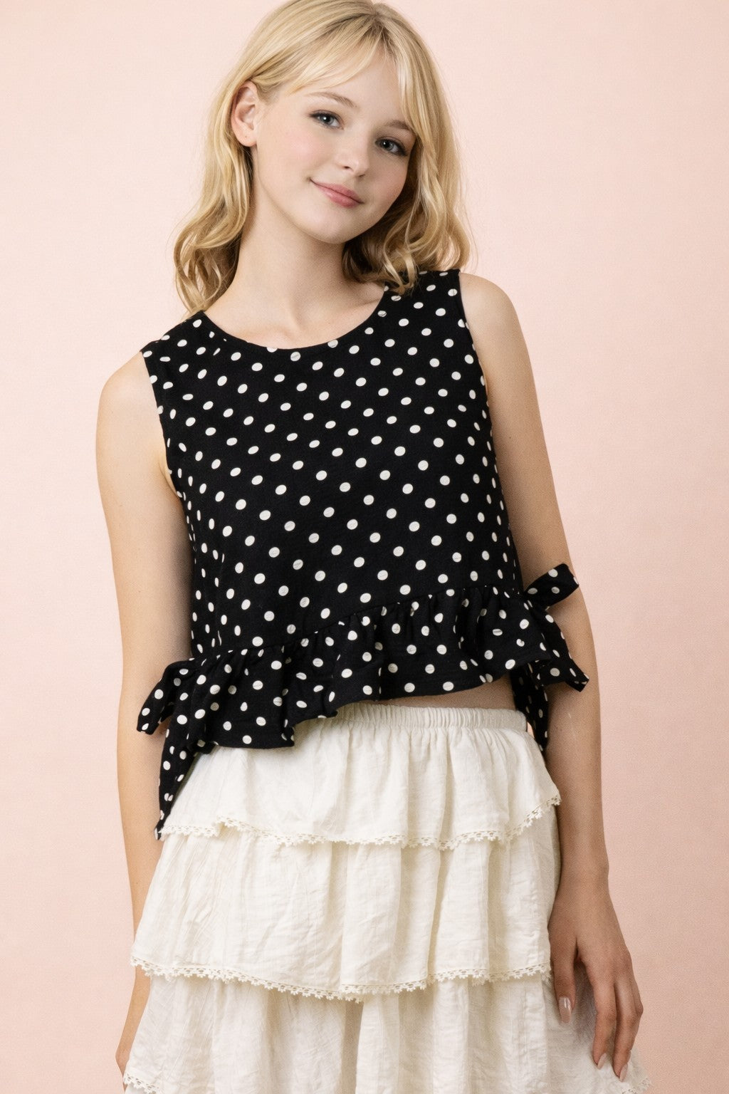 lady wearing black and white polka dot top and white ruffle skirt on tan background