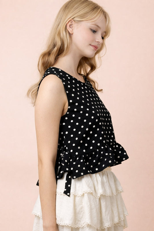 lady wearing black and white polka dot top and white ruffle skirt on tan background