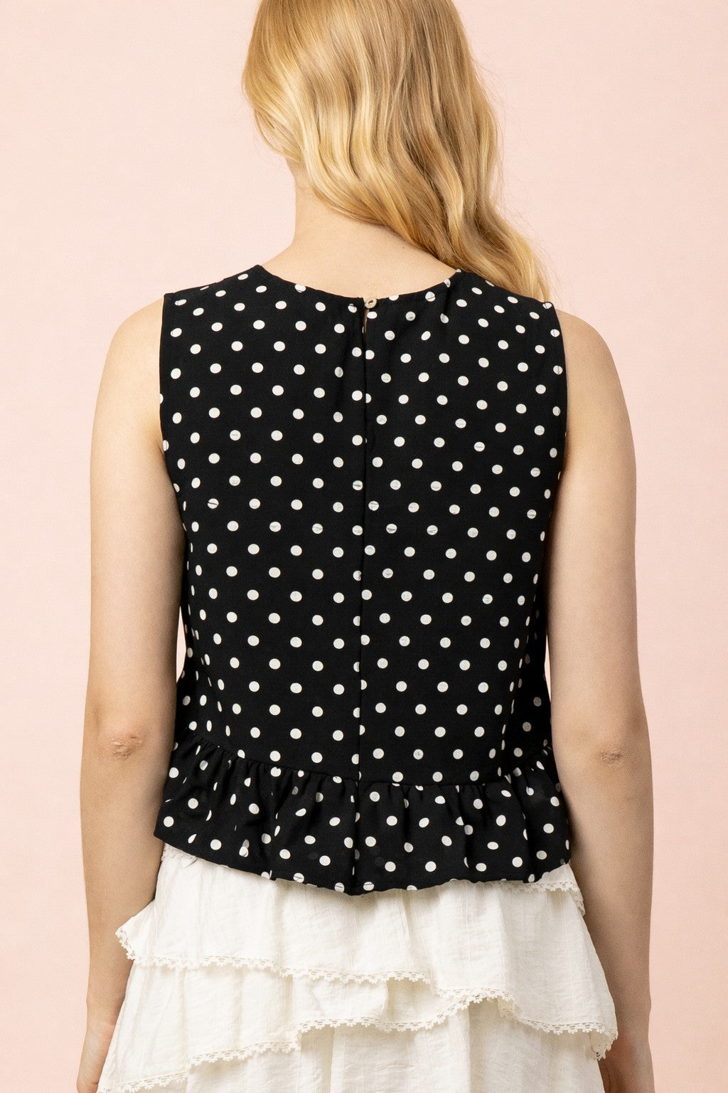 back view - lady wearing black and white polka dot top and white ruffle skirt on tan background