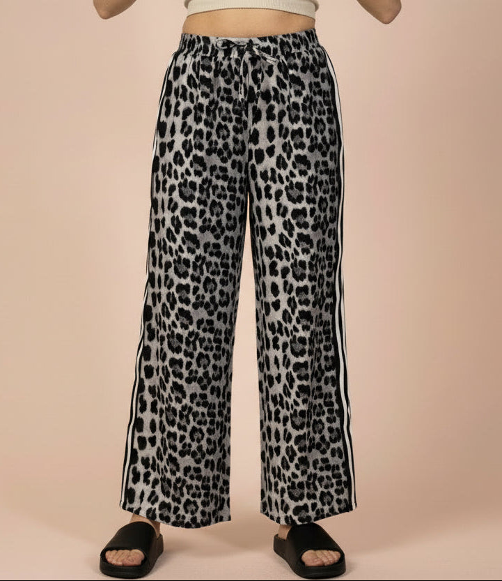 Leopard print pants with side stripes worn by a person on a beige background