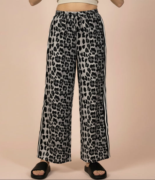 Leopard print pants with side stripes worn by a person on a beige background