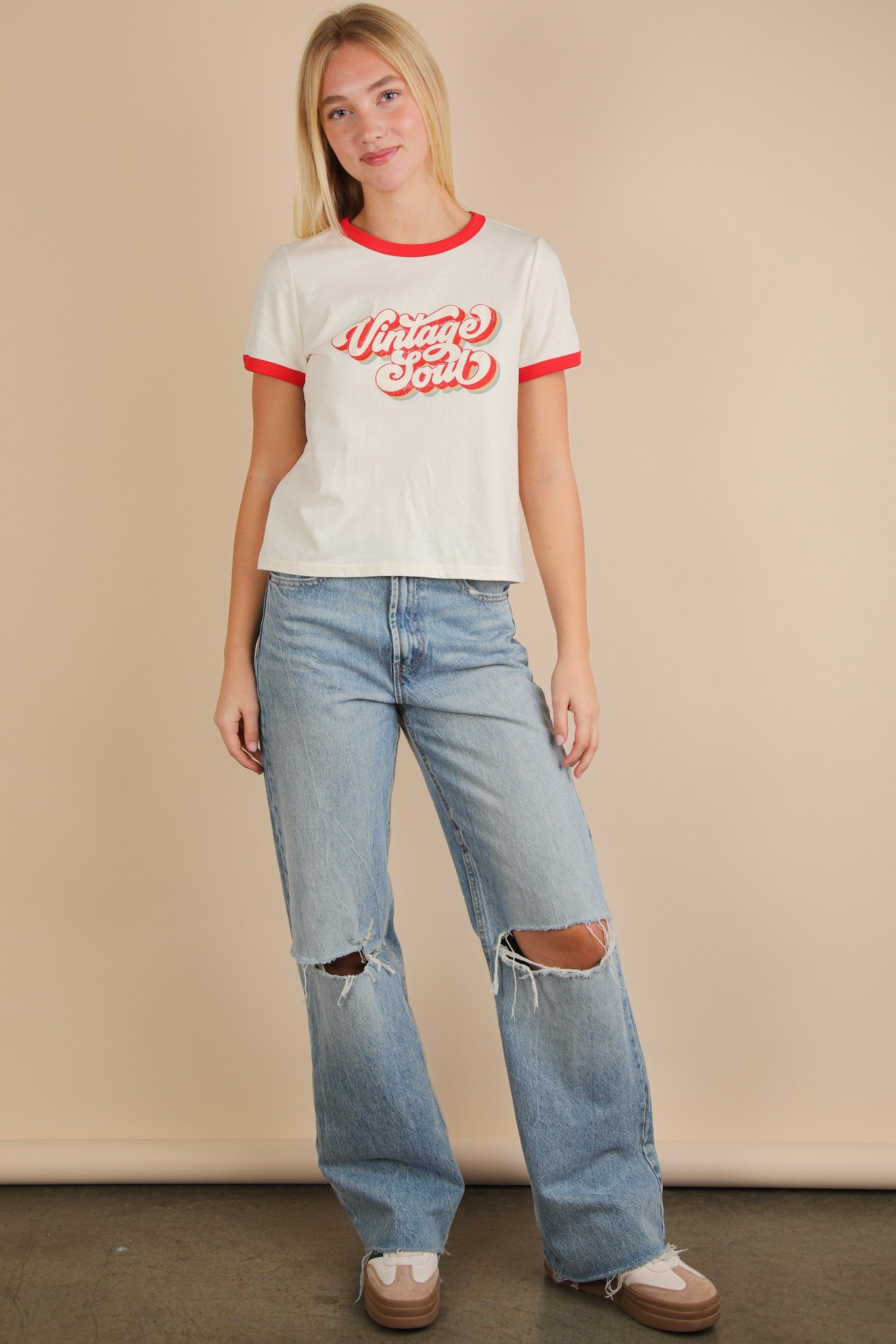 Woman wearing a white t-shirt with red text and ripped jeans against a beige background