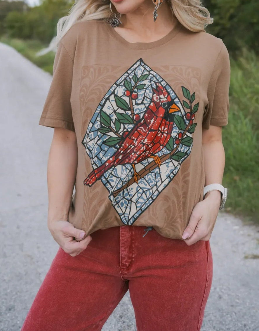 Woman wearing a brown t-shirt with a stained glass cardinal design outdoors.