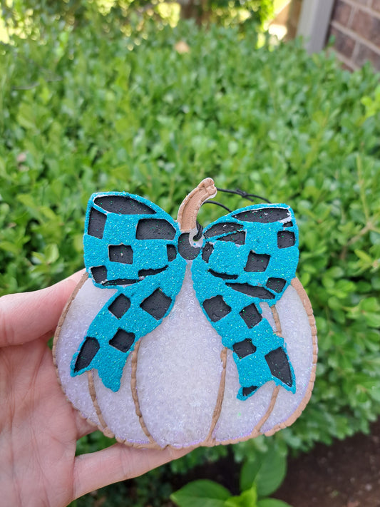white pumpkin freshie with blue and black checkered bow held in a hand on a green background