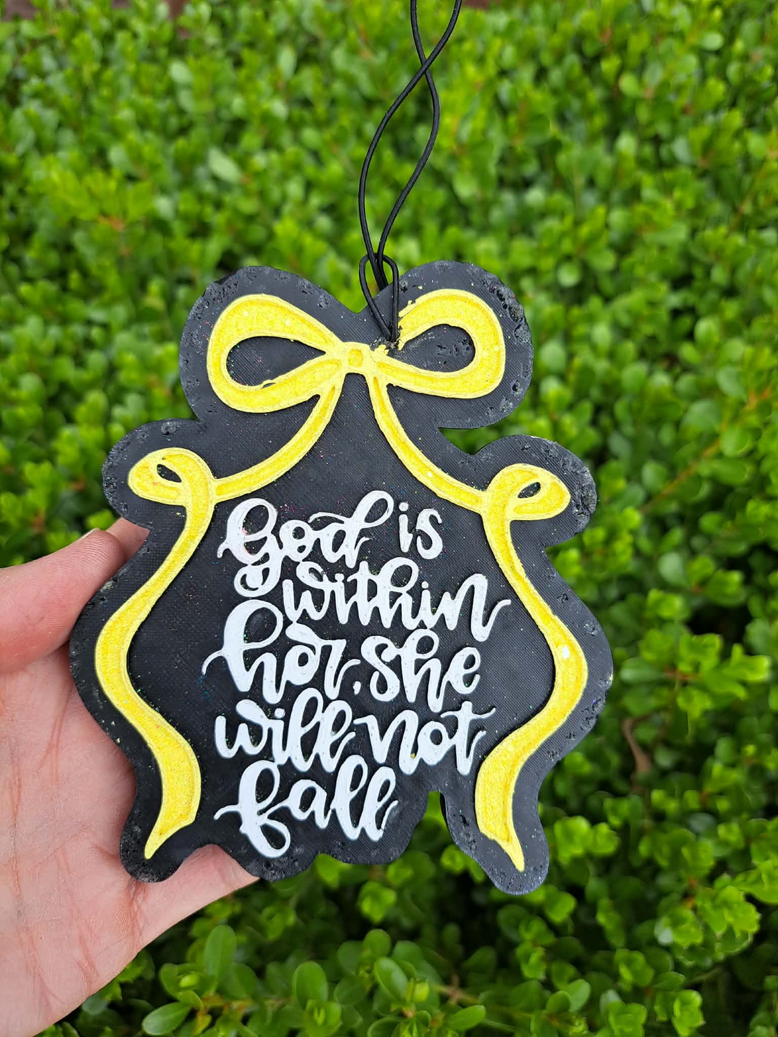 Decorative freshie with text and yellow bow against a green bush background