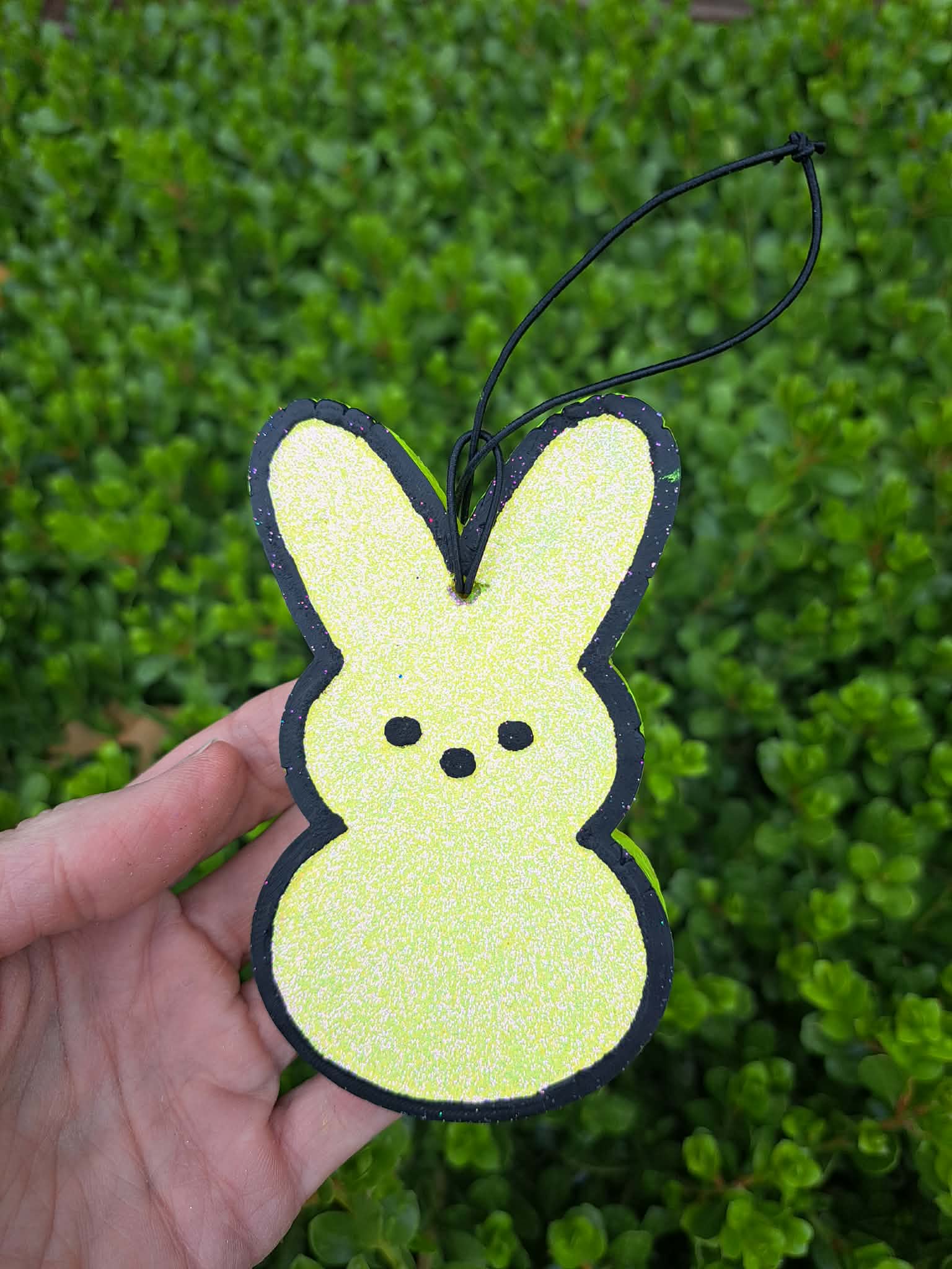 Hand holding a yellow decorative bunny shaped air freshener against a green leafy background