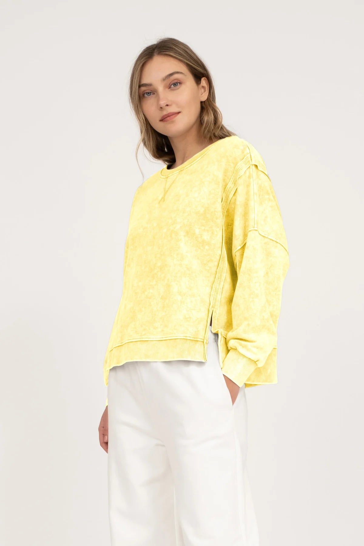 woman wearing a yellow acid washed top with white pants on a neutral background