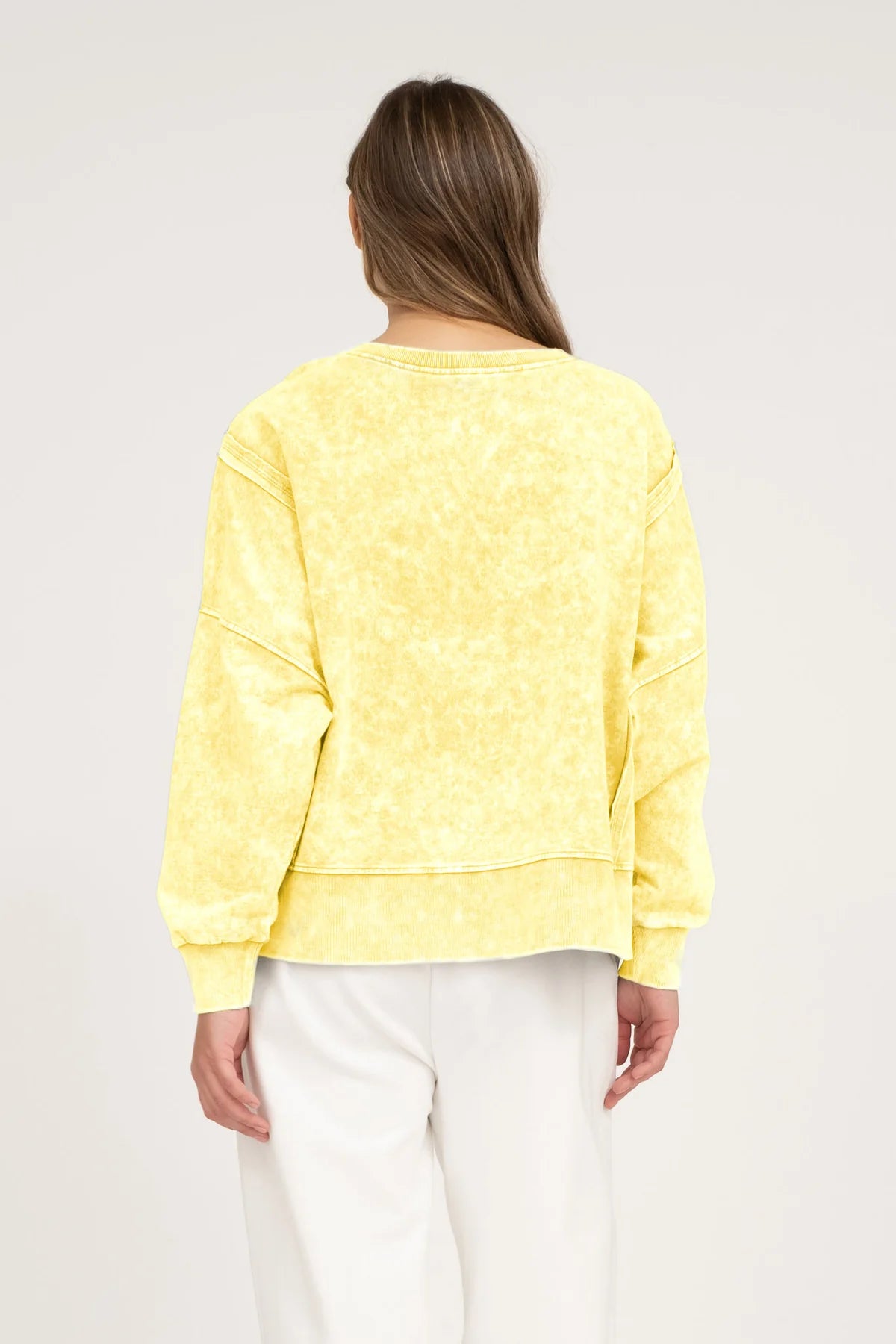 back view of a woman wearing a yellow acid washed top on a netural background