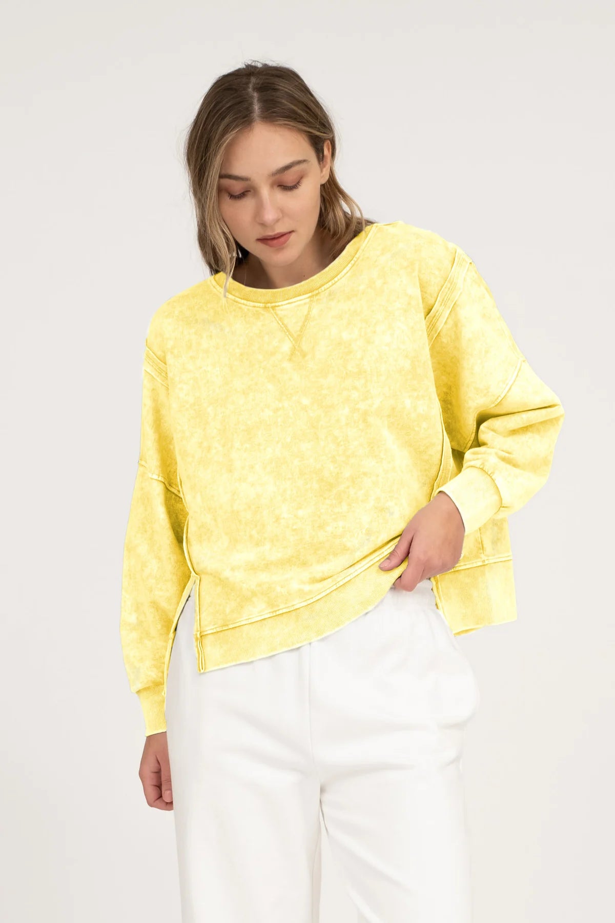 woman wearing an exposed seam yellow top and white pants on a neutral background