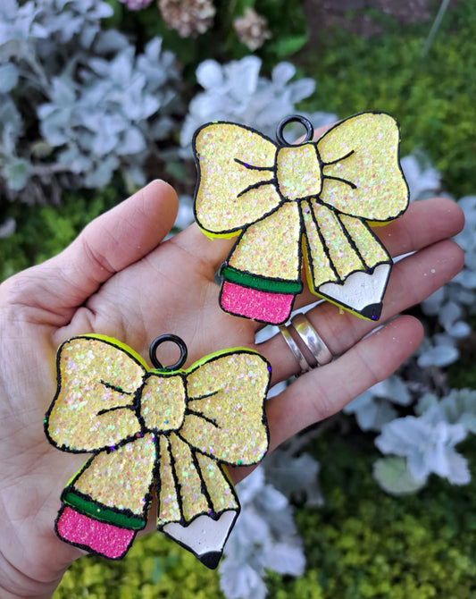 Hand holding two glittery bow-shaped freshies with a natural background