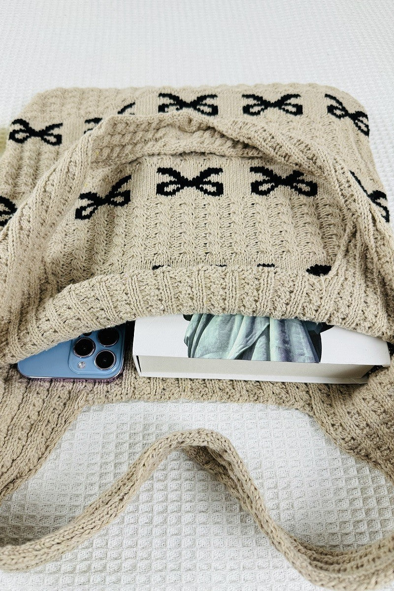 Knitted beige blanket with black bows draped over a white surface