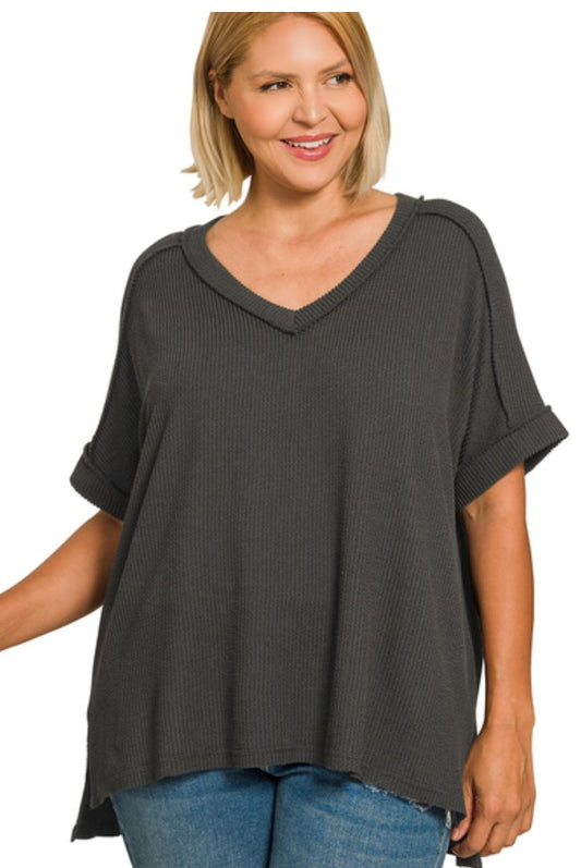 Woman wearing a dark gray textured top and blue jeans on a white background
