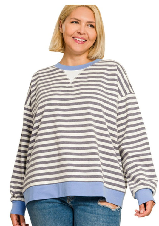 A woman wearing a charcoal and cornflower blue horizontally striped long-sleeve sweatshirt with solid blue ribbed trim, paired with blue jeans, against a plain white background.