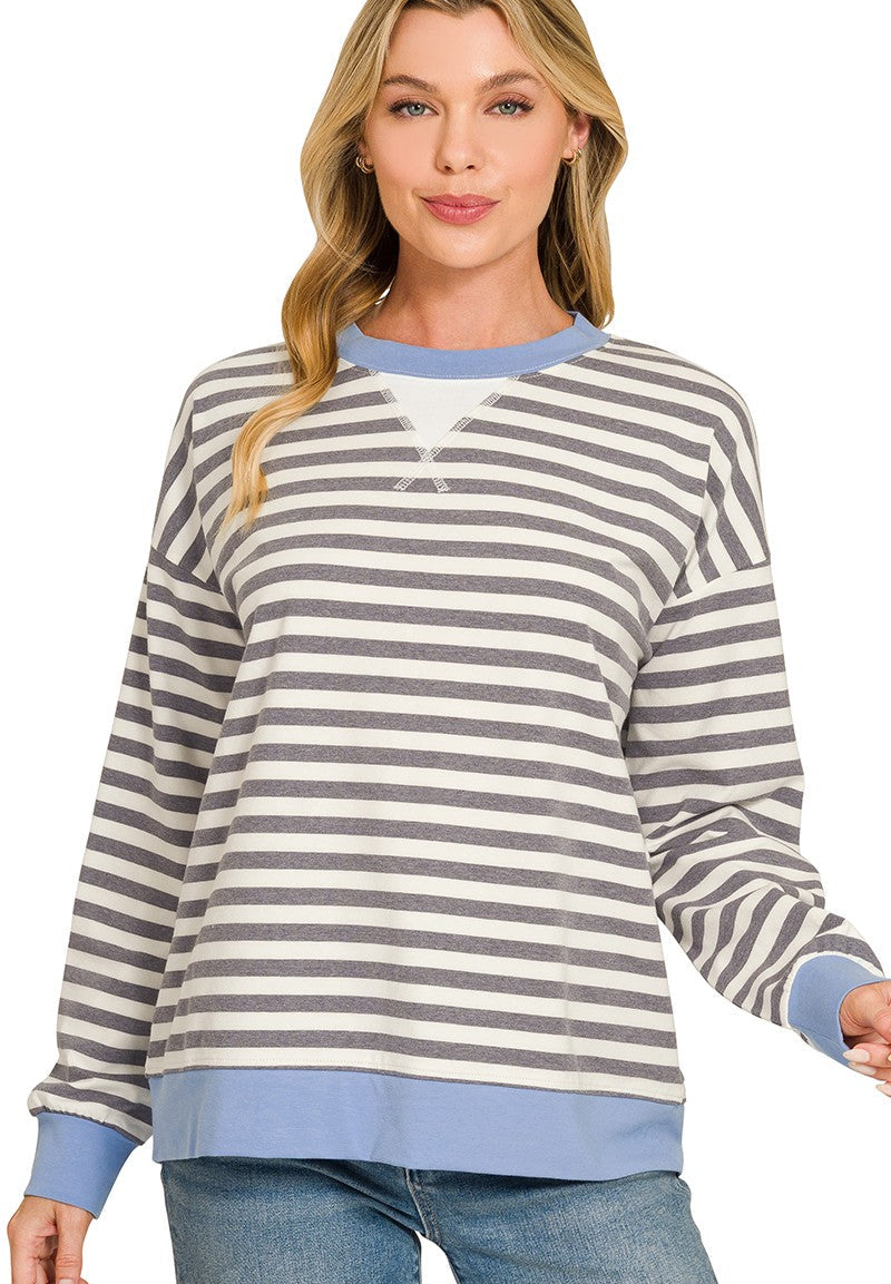 A woman wearing a charcoal and cornflower blue horizontally striped long-sleeve crewneck sweatshirt with solid blue ribbed trim, paired with blue jeans, against a plain white background.