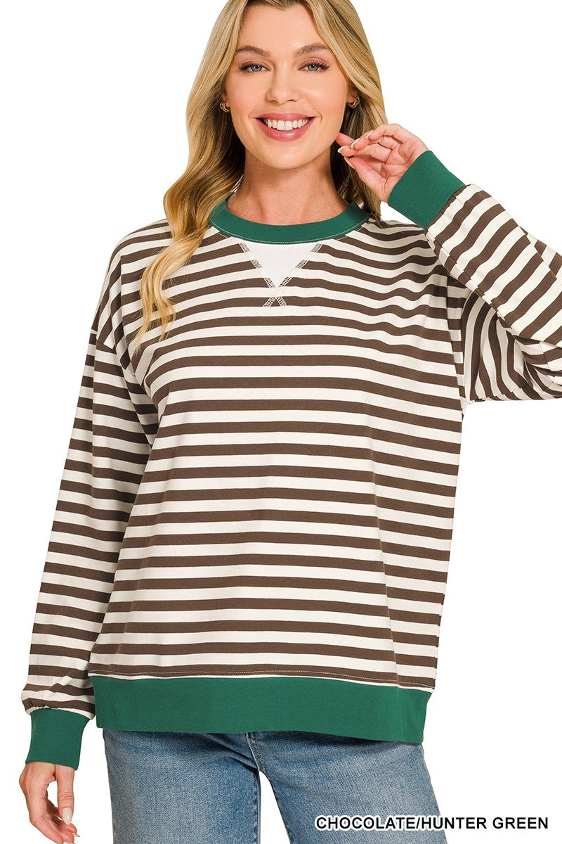 A woman wearing a long-sleeve crewneck sweatshirt with horizontal brown and cream stripes, accented with solid green ribbed trim at the collar, cuffs, and hem, paired with blue jeans against a white background.
