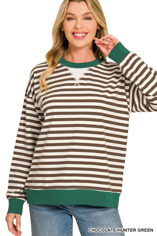 A woman wearing a long-sleeve crewneck sweatshirt with horizontal brown and cream stripes, accented with solid green ribbed trim at the collar, cuffs, and hem, paired with blue jeans against a white background.