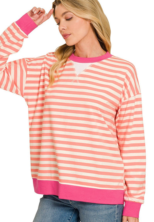 A woman wearing a coral and pink striped long-sleeve crewneck sweatshirt with solid pink ribbed trim, paired with blue jeans, against a white background.