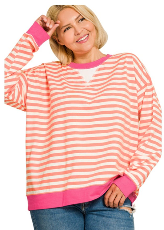 A woman wearing a long-sleeve crewneck sweatshirt with horizontal peach and white stripes, featuring bright pink trim on the collar, cuffs, and hem, paired with blue jeans against a white background.